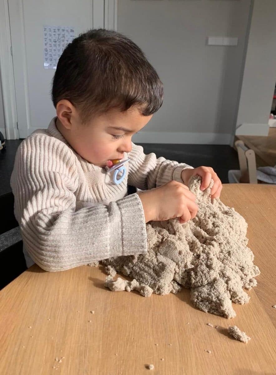 Een kind speelt geconcentreerd met kinetisch zand aan tafel